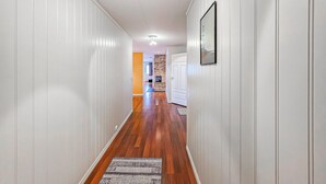 A hallway with wooden flooring, white walls, and a fireplace in the background.