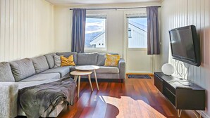 A living room with a grey sofa, a small round table, a TV, and a wooden floor.