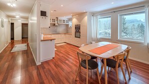 A modern kitchen with wooden cabinets, a dining table with chairs, and large windows with a snowy view.