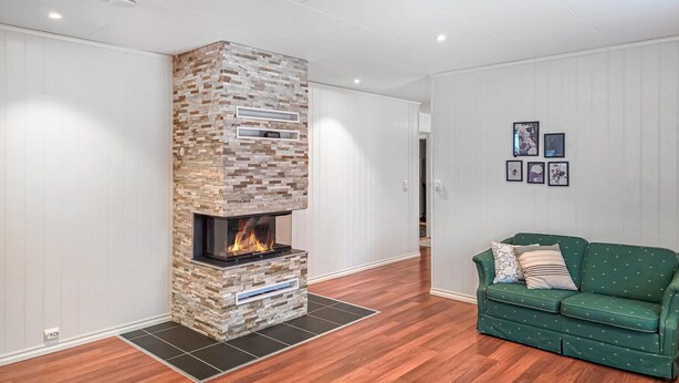 A modern living room with a stone fireplace, wooden flooring, and a green sofa.