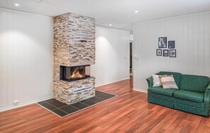 Een moderne woonkamer met een stenen open haard, houten vloeren en een groene bank.