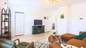 Een moderne woonkamer met een televisie, een groene mediakast en een gezellig zithoekje met een kamerkleed.