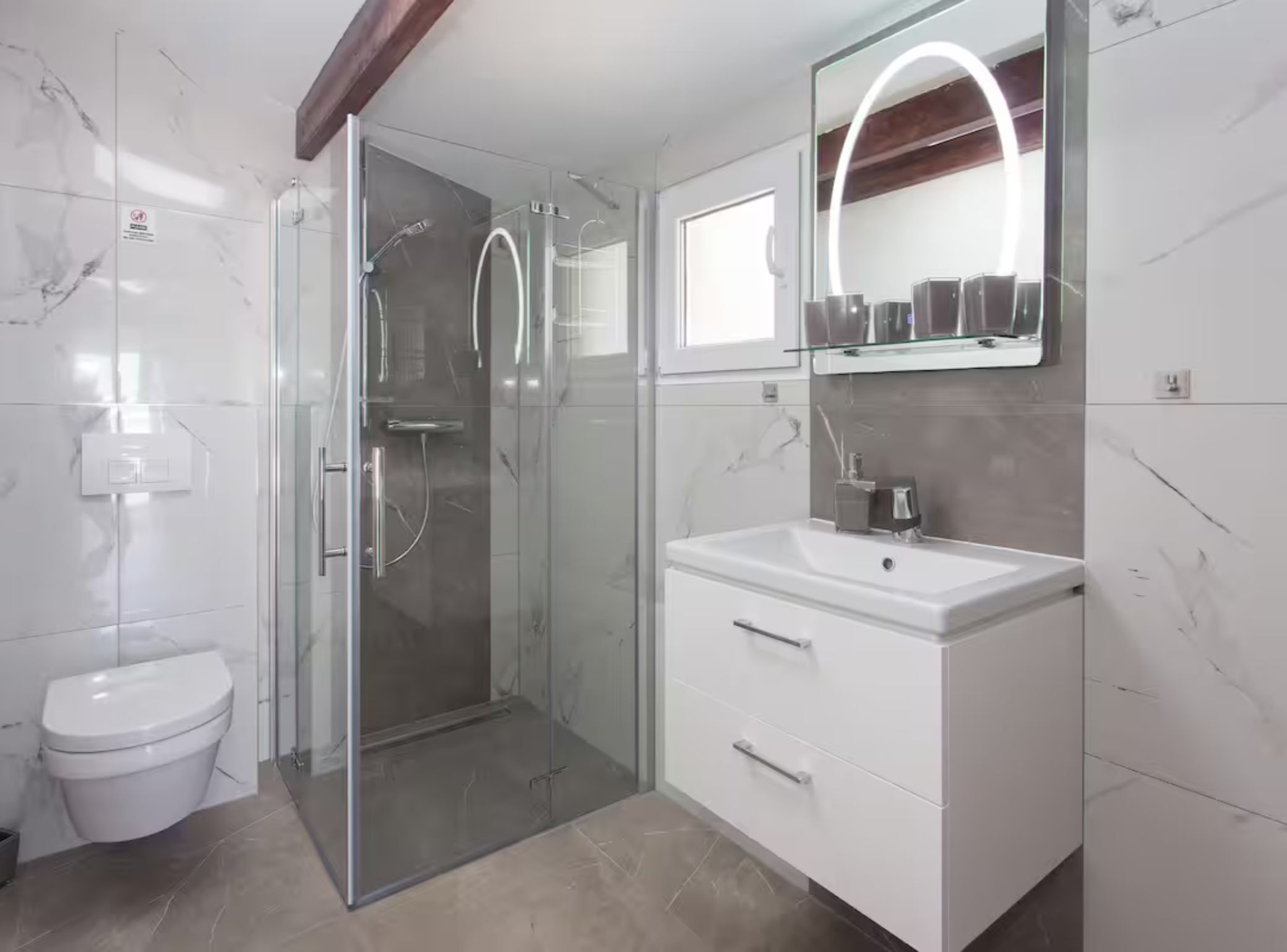 Un baño moderno con ducha de vidrio, inodoro blanco y tocador con espejo.