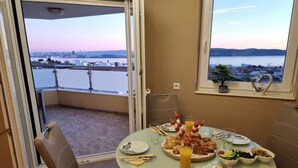 A dining area with a table set for four, overlooking a cityscape and water body. - Villa Rocco del Mare (Kastela)
