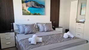 A bedroom with a large bed, two nightstands, a wardrobe, and a painting of a coastal landscape. - Villa Rocco del Mare (Kastela)