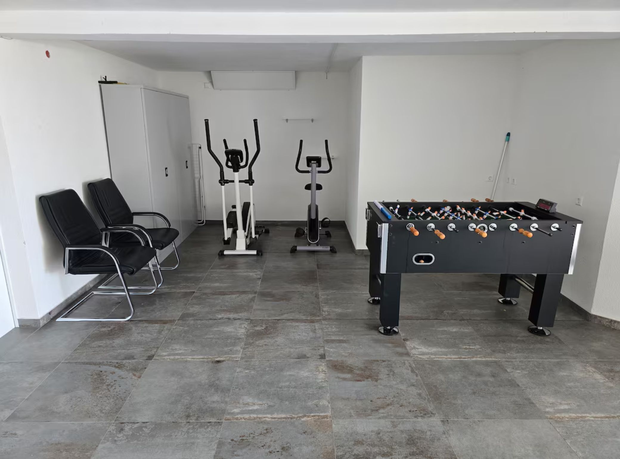 Ein Raum mit einem Kicker, zwei Ergometer und schwarzen Stühlen.