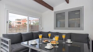 A breakfast setup with a glass table, grey sofa, and a view of buildings outside. - Villa Rocco del Mare (Kastela)