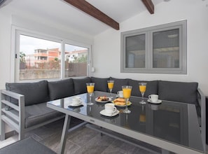 A breakfast setup with a glass table, grey sofa, and a view of buildings outside. - Villa Rocco del Mare (Kastela)