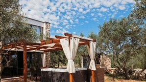 A hot tub under a wooden pergola with a stone wall backdrop, surrounded by olive trees. - Capesanta (Preko)