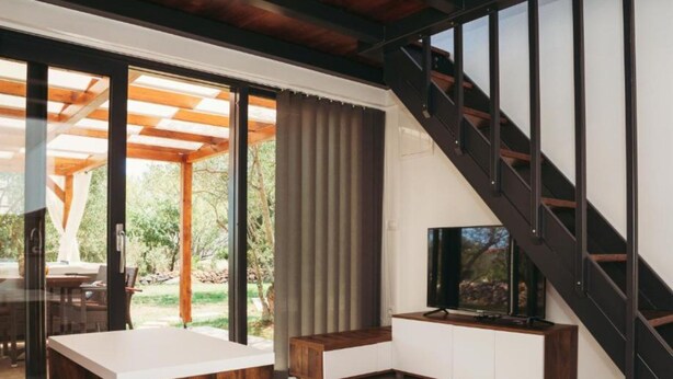 A modern living room with a TV, wooden furniture, a glass door leading to a patio, and a staircase. - Capesanta (Preko)