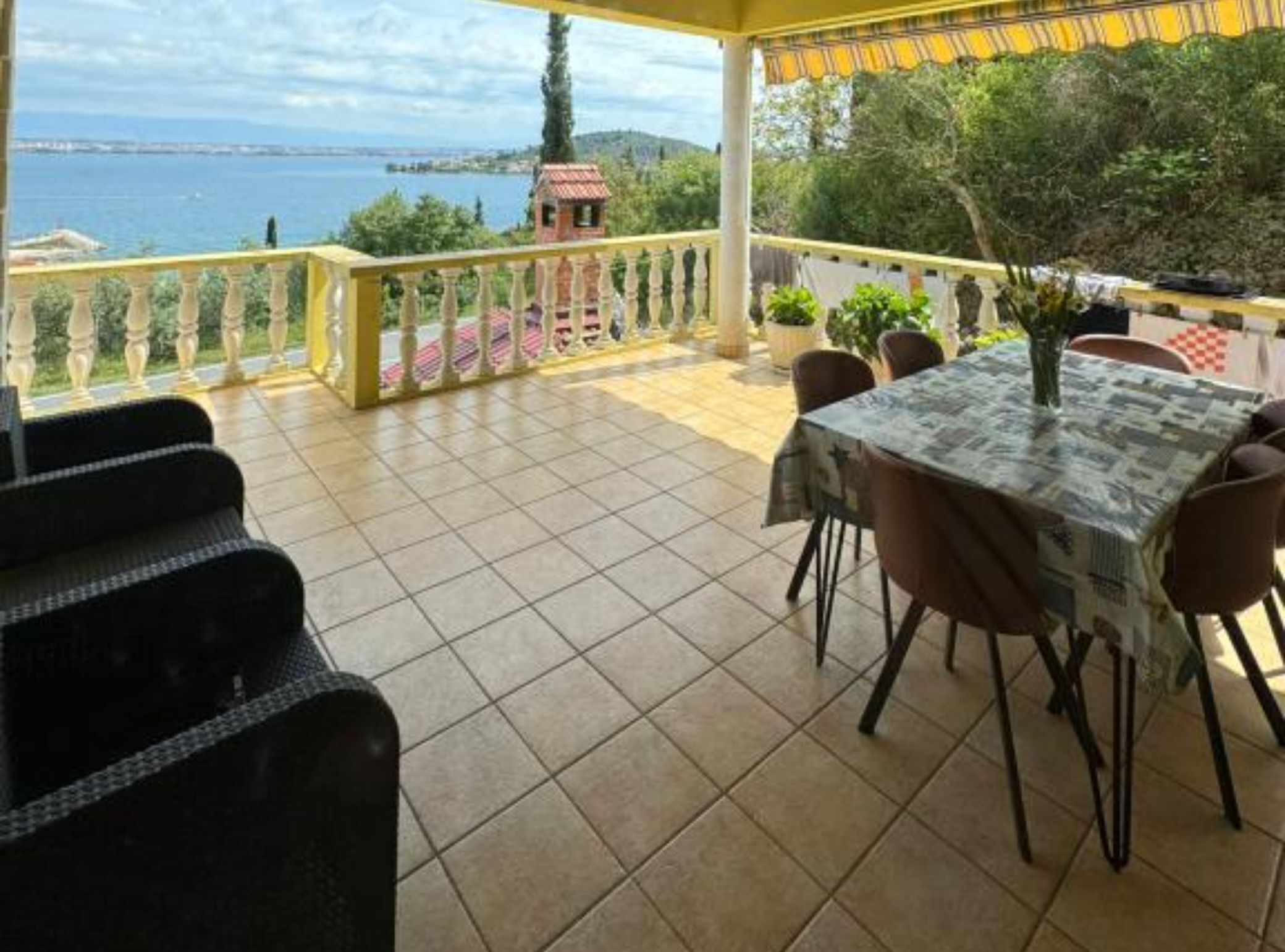 A terrace with a table and chairs, a view of the sea, and a small tower in the background.