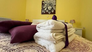A neatly made bed with a purple pillow and a stack of white towels. - Family Apartment Sofija (Preko)