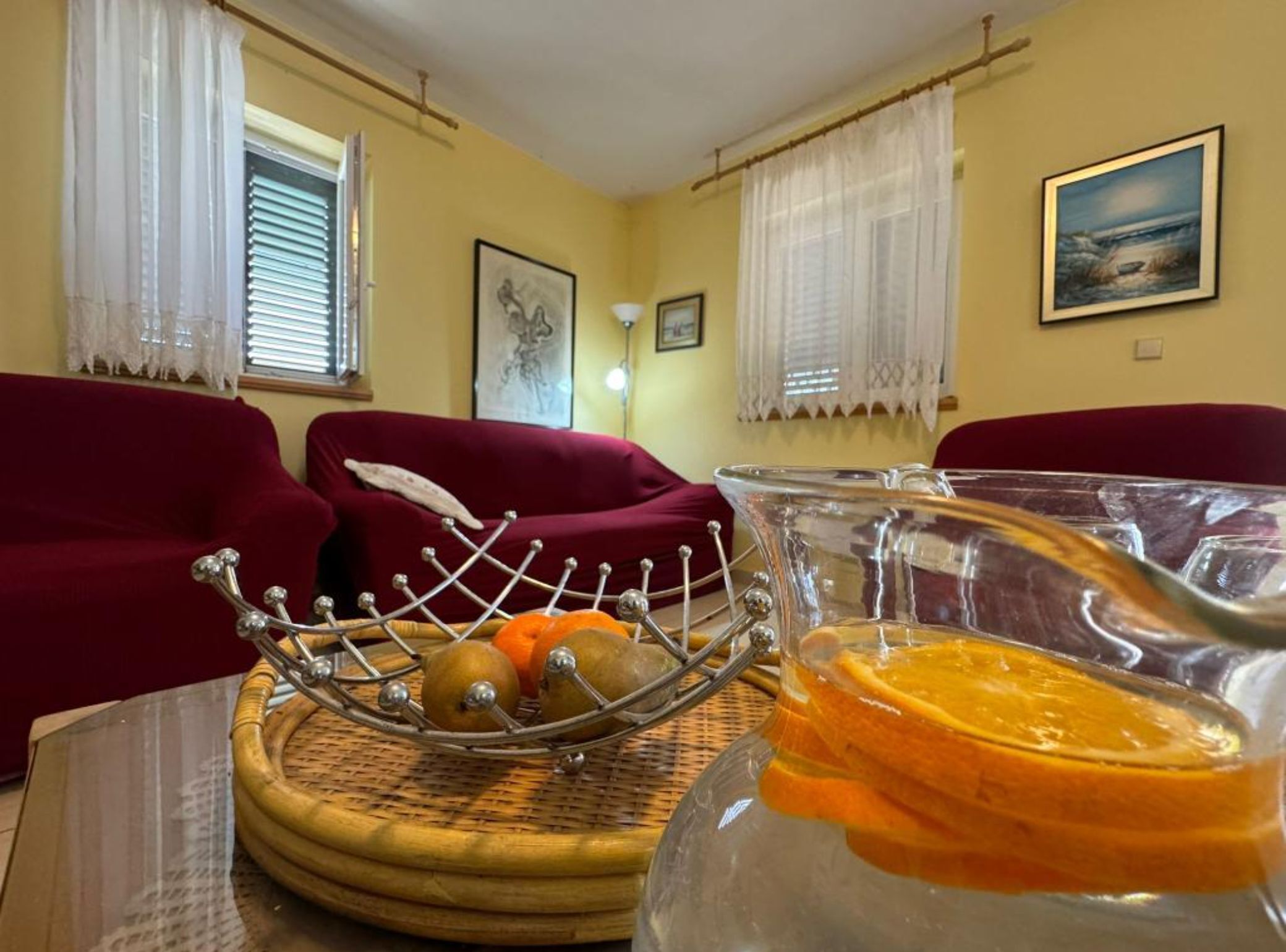 Un salon avec un canapé rouge, un saladier en verre rempli d’oranges et un tableau accroché au mur.