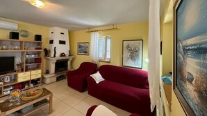 A living room with a fireplace, a red sofa, a coffee table with fruits, and a painting on the wall. - Family Apartment Sofija (Preko)