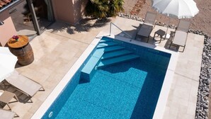 A rectangular swimming pool with a clear blue tile interior, surrounded by a stone deck. There are lounge chairs and a white umbrella providing shade. - Villa Ulika With Pool (Malinska-Dubasnica)