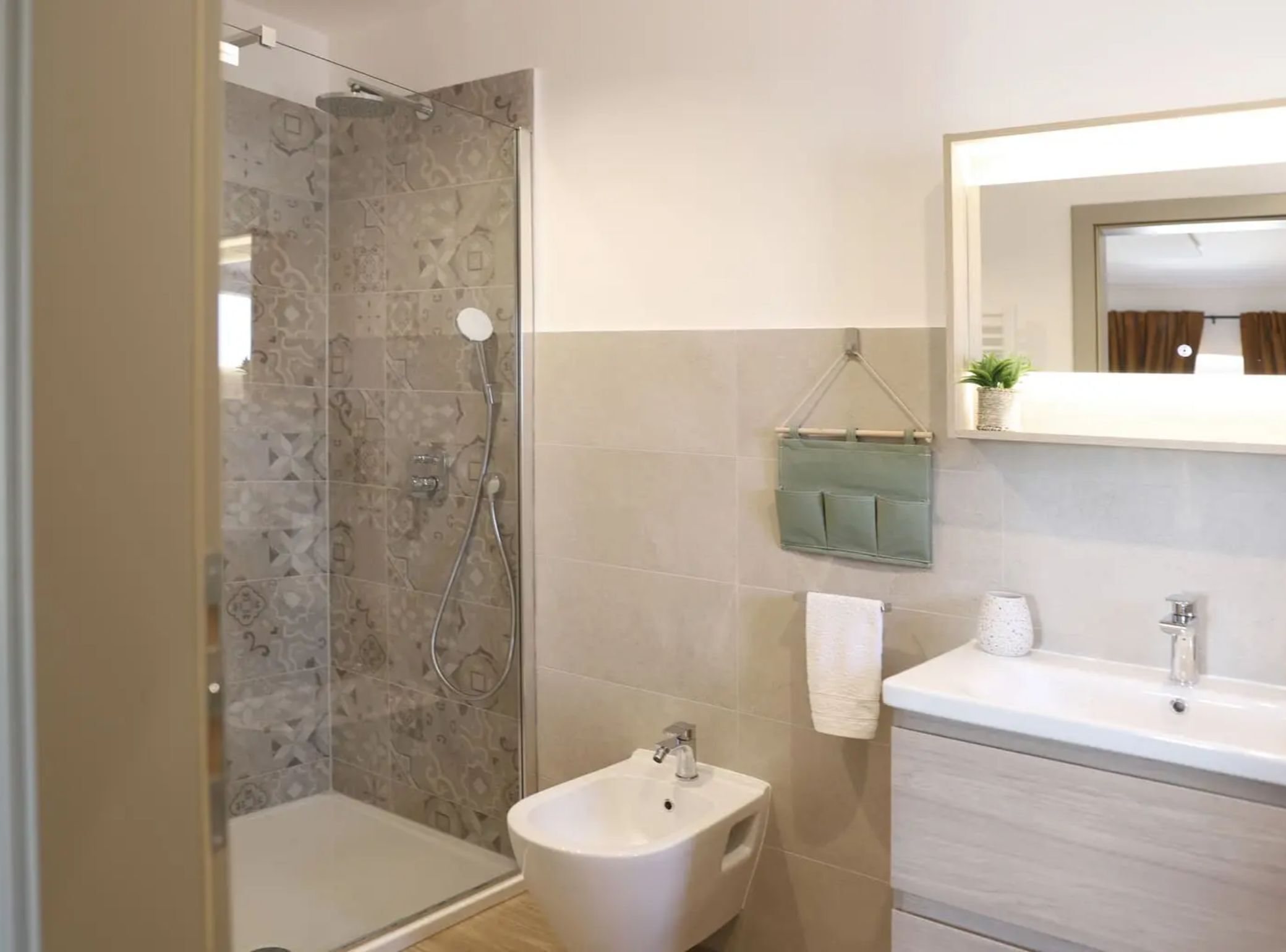 Een moderne badkamer met een douche, een toiletgondel, een wastafel en een spiegel.