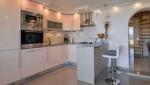 A modern kitchen with stainless steel appliances, a central island with bar stools, and a view of a wooden staircase. - Holiday Home Luka Topličica (Novi Marof)