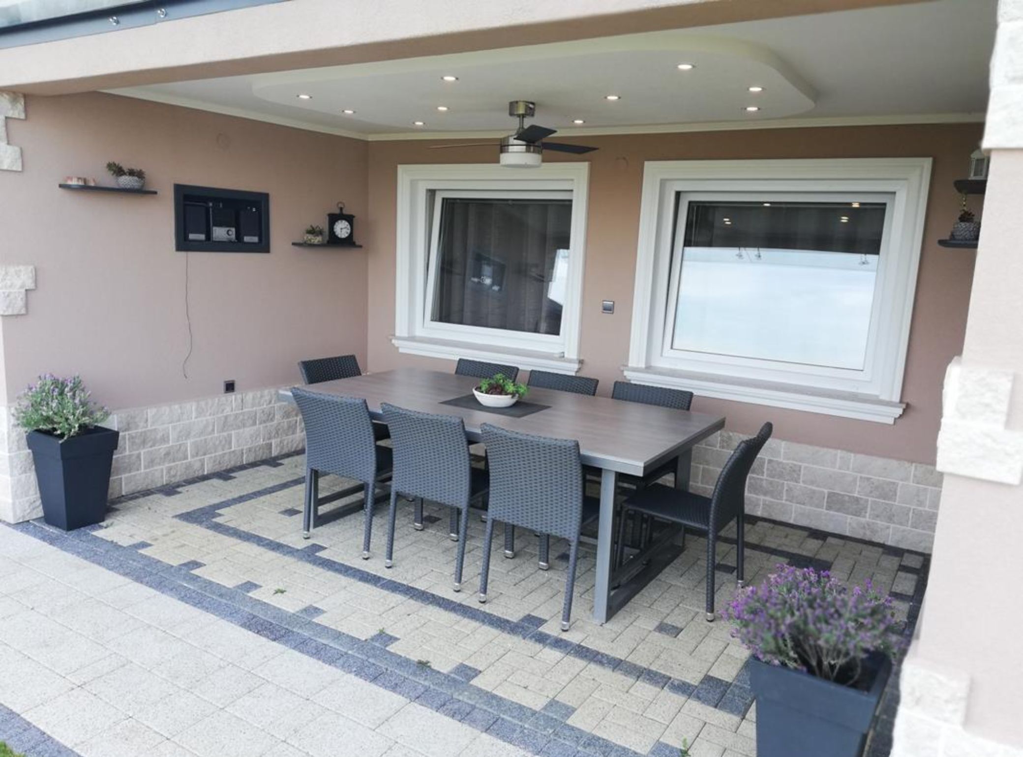 Eine Terrasse im Freien mit Esstisch und Stühlen, einem Deckenventilator und einem großen Fenster.