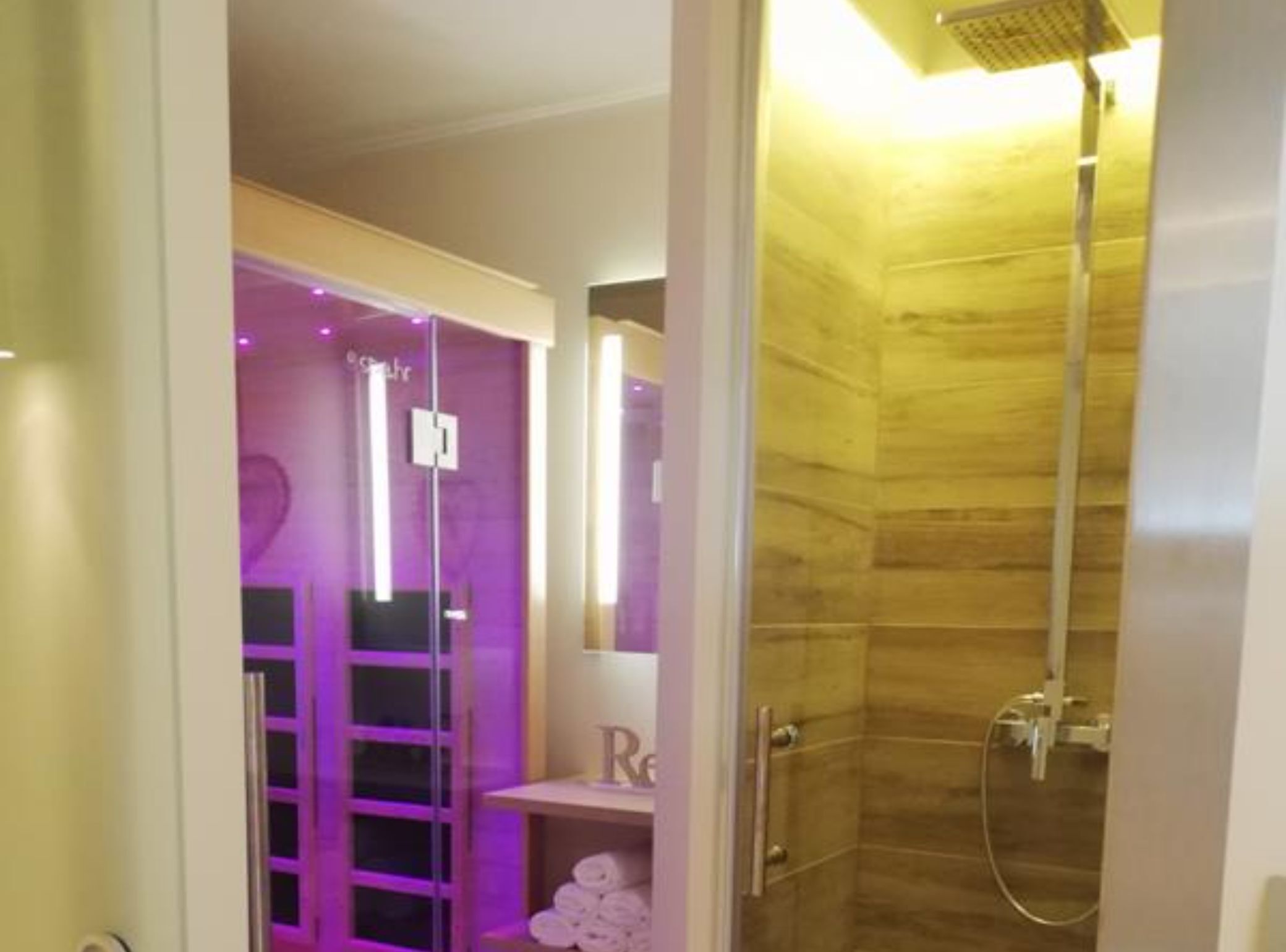 A modern bathroom with a glass shower enclosure, a vanity with a mirror, and a shelf with towels.