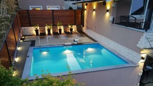 A rectangular swimming pool with a wooden deck and lounge chairs, surrounded by a brick wall and a wooden fence. - Holiday Home Luka Topličica (Novi Marof)