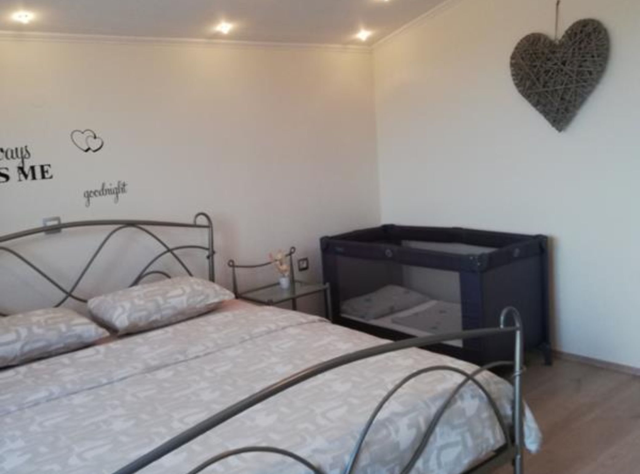 Un dormitorio con una cama, una mesita pequeña y una decoración de corazón en la pared.