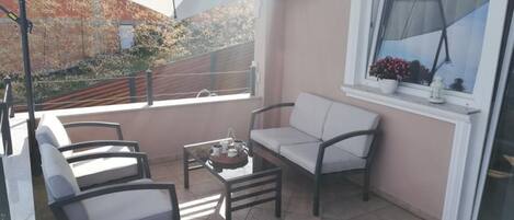 A balcony with a sofa, chairs, and a table with a tray of cups and a teapot.