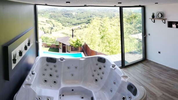 A modern bathroom with a large bathtub, a glass shower enclosure, and a view of a mountainous landscape. - Holiday Home Luka Topličica (Novi Marof)