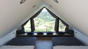 A small, triangular attic bedroom with two beds, a window with curtains, and a view of a green landscape. - Holiday Home Luka Topličica (Novi Marof)