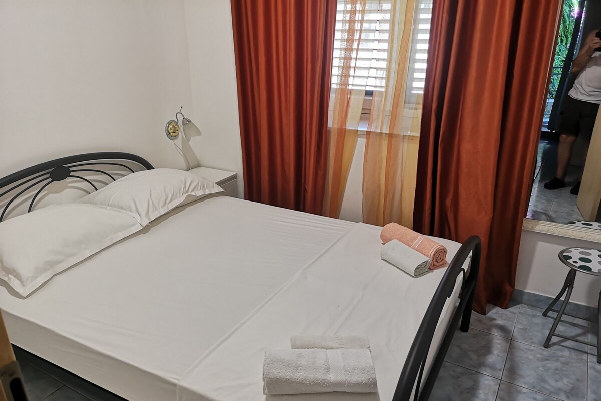 A neatly made bed with white linens, a small bedside table with a lamp, and a window with curtains.