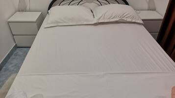 Una cama con ropa blanca, dos mesitas de noche y una lámpara de pared.
