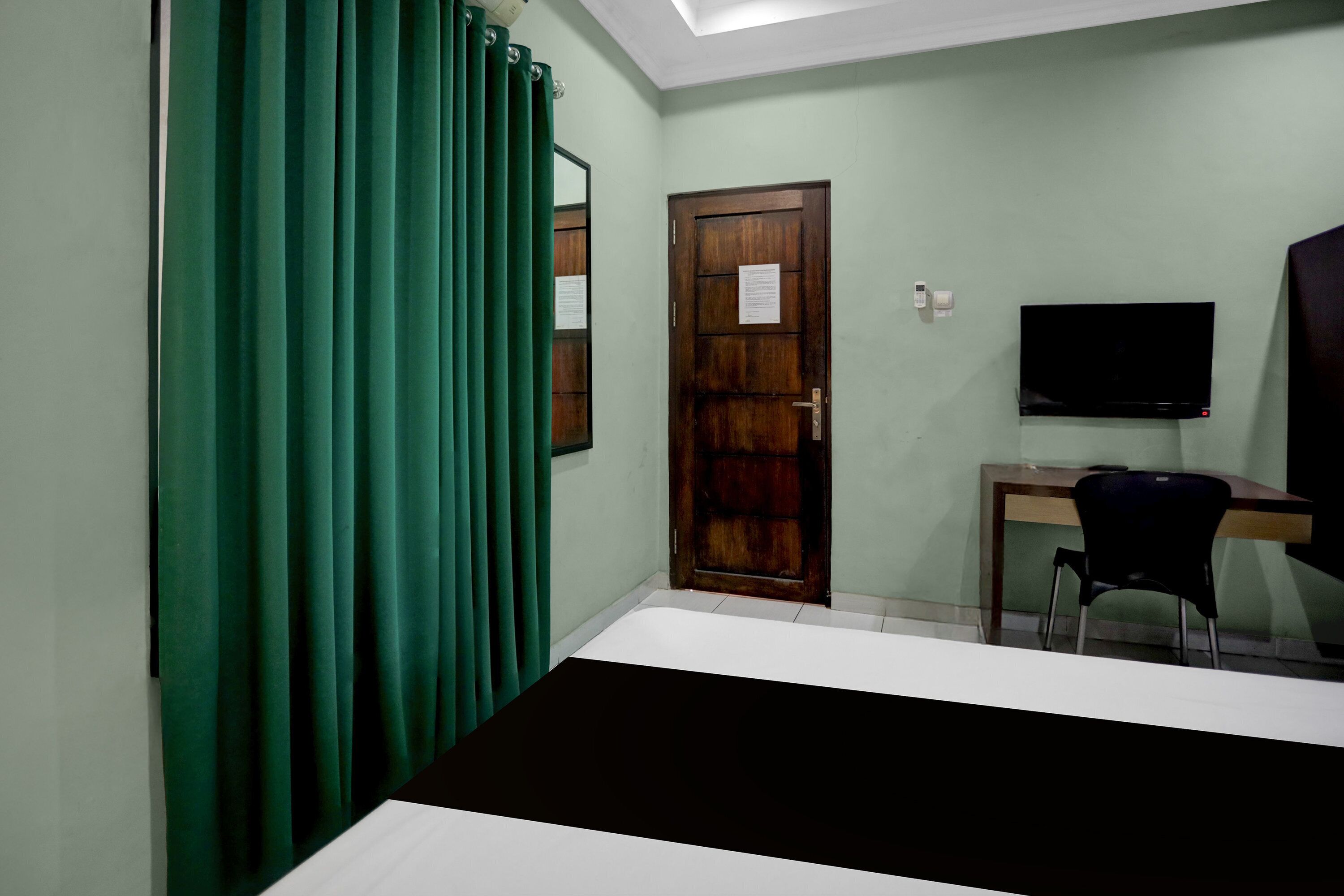 A room with a bed, a desk with a chair, a television, and a door with a notice.