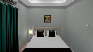 Une chambre à coucher avec un lit, des rideaux verts, une lampe fixée au mur, un lustre et un petit tableau.