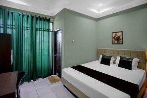 A hotel room with a bed, a desk, a chair, a window with curtains, and a wall-mounted picture. - Hotel O near Museum Lambung Mangkurat (Banjarbaru)