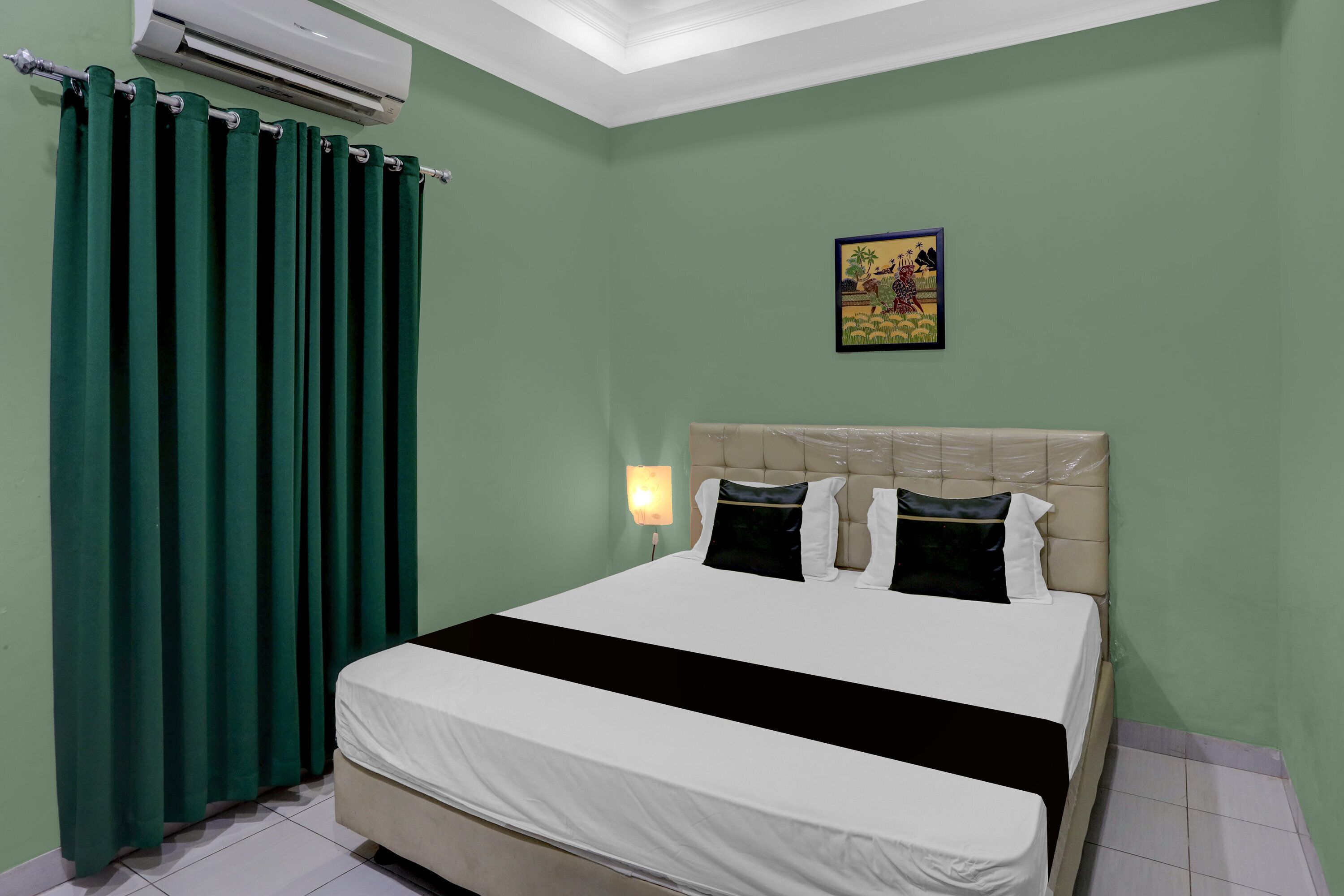 Una habitación con cama, cortinas verdes, aire acondicionado instalado en la pared y una lámpara fija en la pared.
