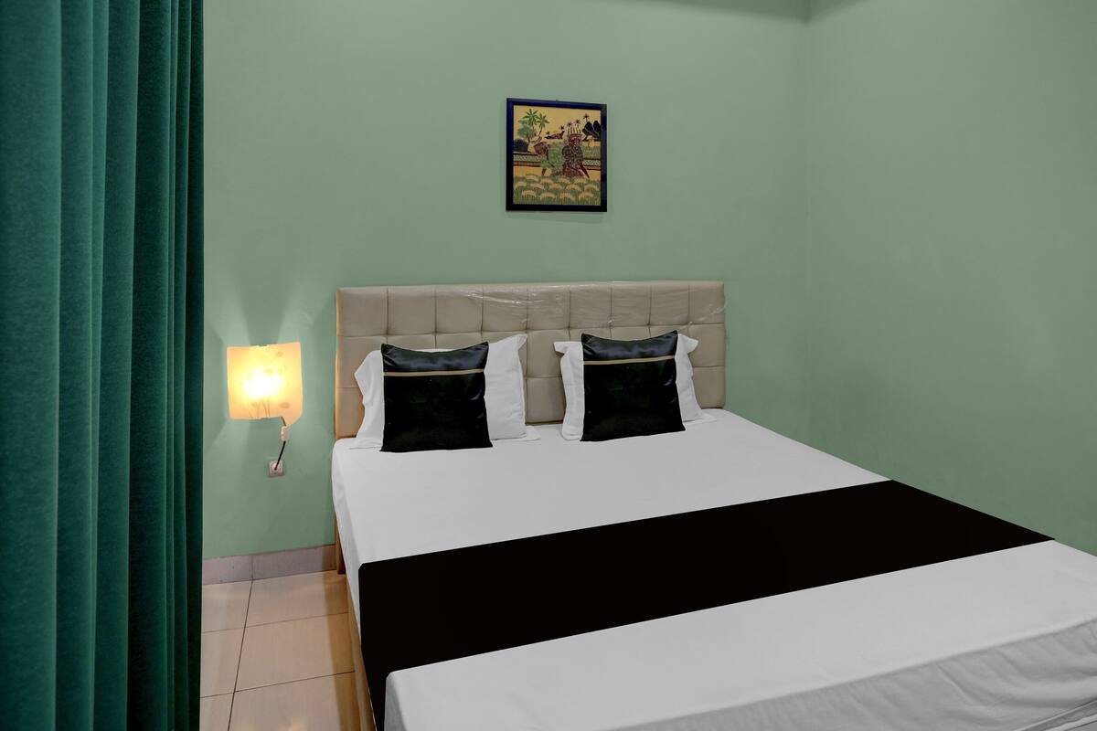 Ein Hotelzimmer mit einem Bett, einer Wandleuchte, einem gerahmten Bild und einem grünen Vorhang.