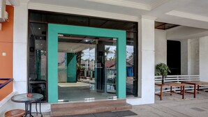 Une entrée d’immeuble avec une porte vitrée, un petit espace extérieur aménagé en coin salon et un intérieur visible à travers la vitre.