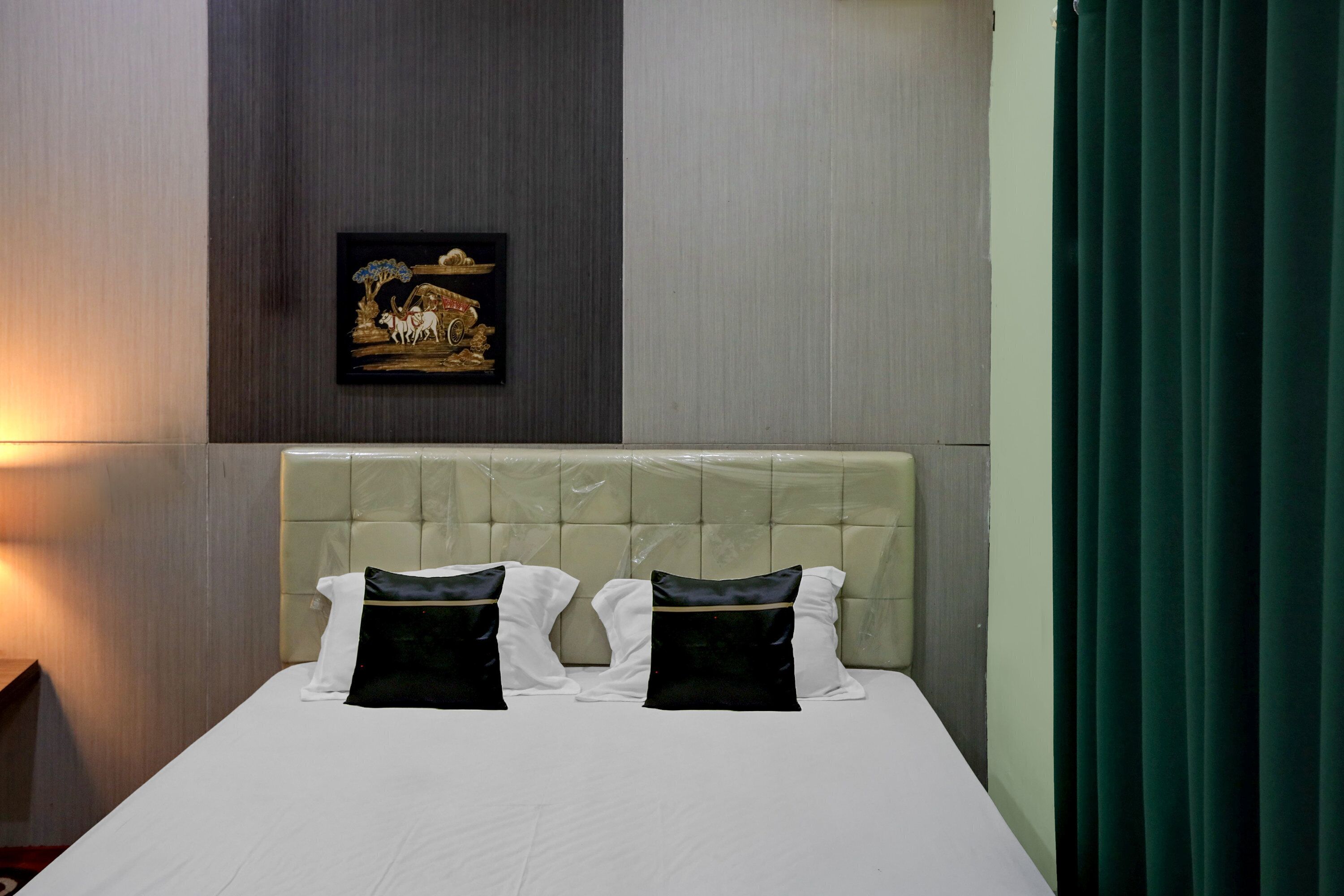 Una habitación de hotel con cama, cabecera, un cuadro enmarcado en la pared y una cortina.