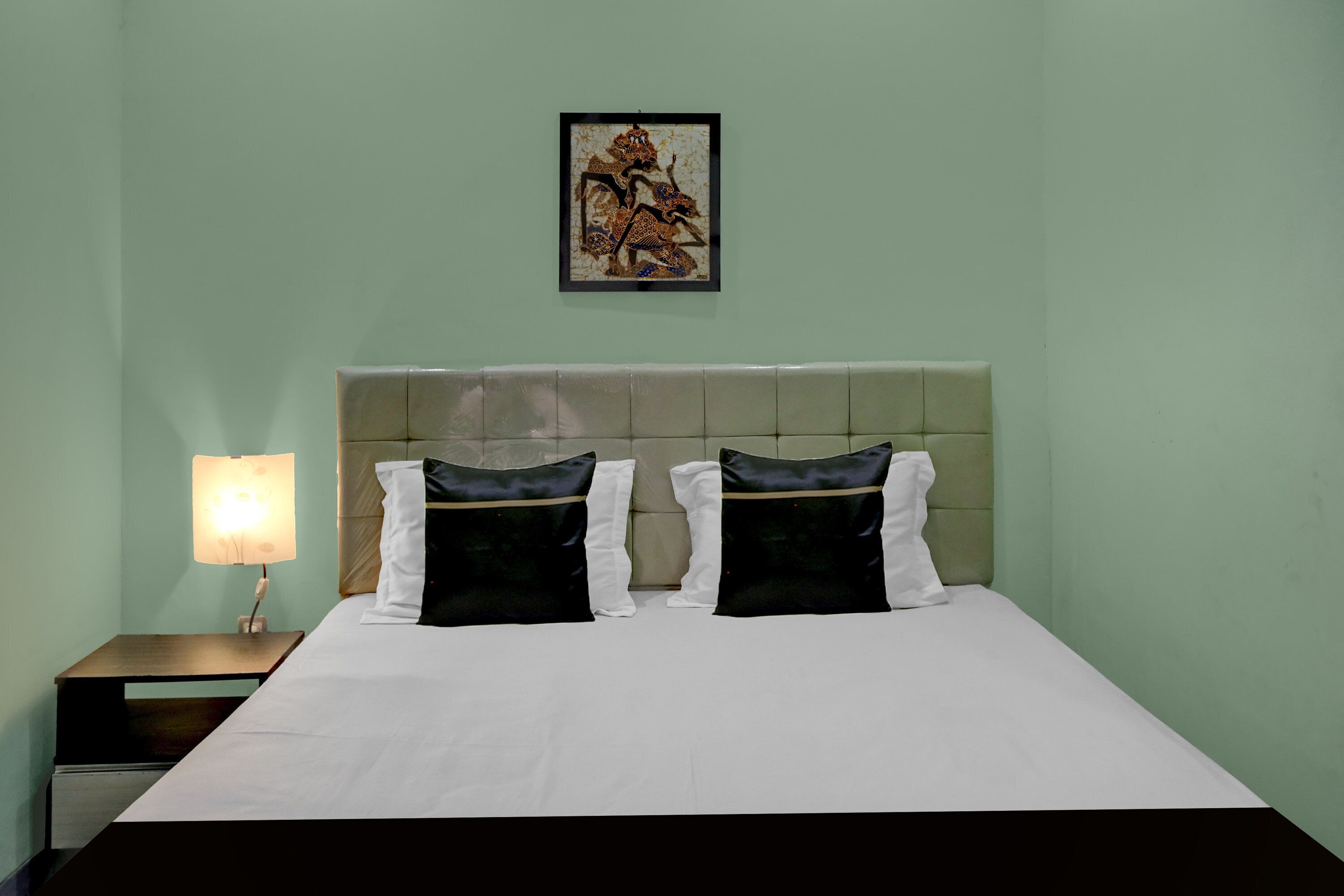 Una habitación de hotel con cama, mesita de noche, lámpara y un cuadro en la pared.