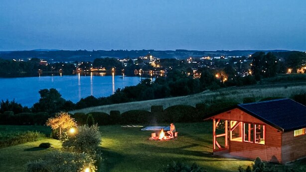 A lakeside property with a wooden cabin, a tent, and a fire pit.