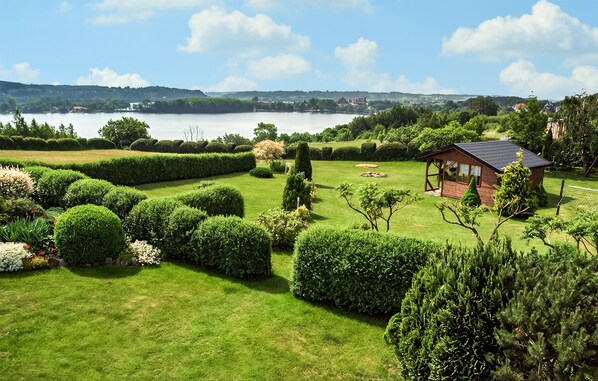 A well-maintained garden with neatly trimmed hedges and a small wooden cabin with a sloped roof. - Amazing apartment in Chmielno with lake view (Chmielno)