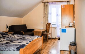 A small, cozy room with a bed, a chair, a table, and a refrigerator. - Amazing apartment in Chmielno with lake view (Chmielno)