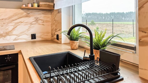 A kitchen with a marble backsplash, a black sink with a faucet, a dish drying rack, and a window with a view of a forest. - Cozy home in Zuromino with WiFi (Zuromino)