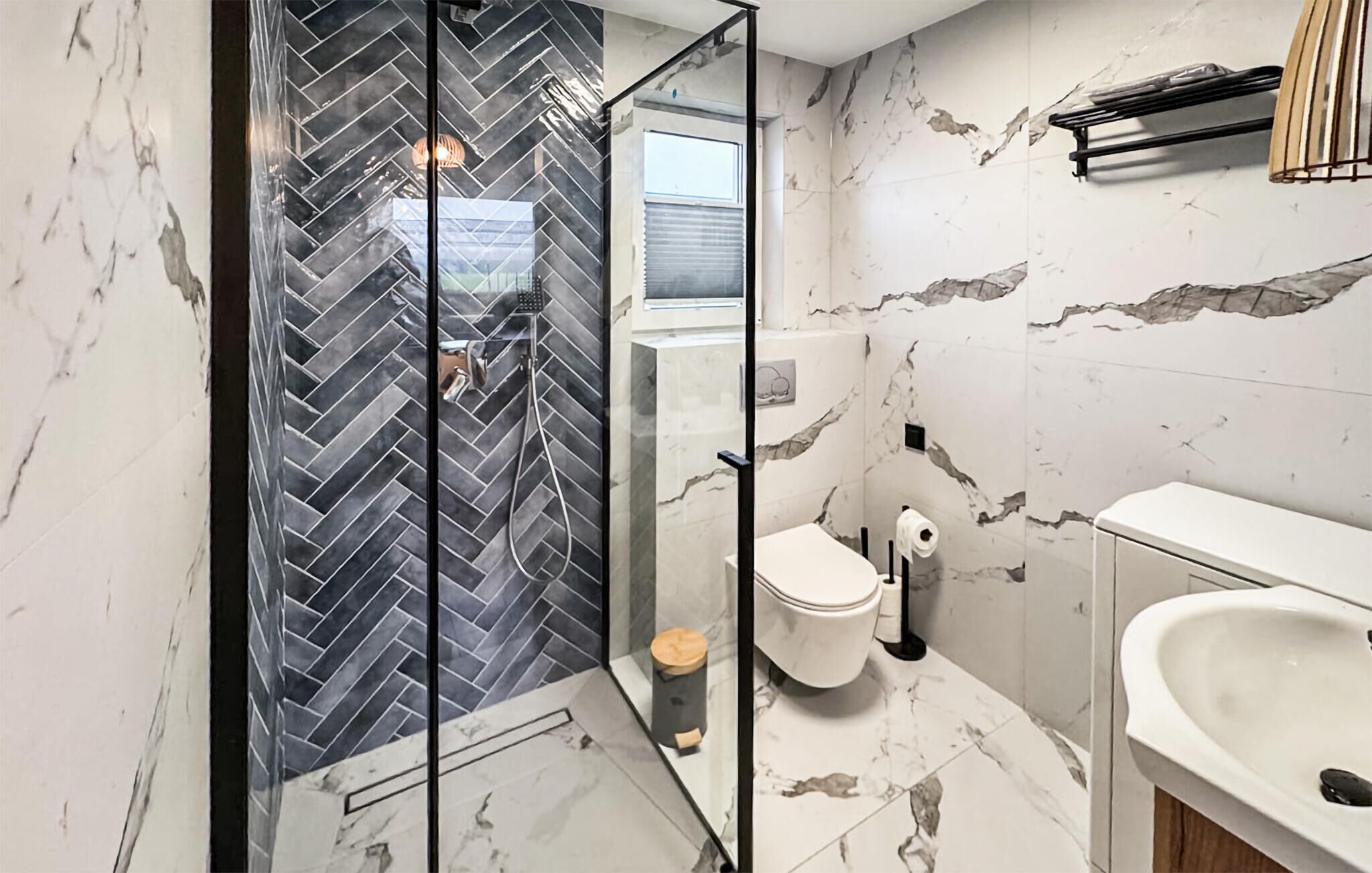 Ein modernes Badezimmer mit Duschwand in Fischgrätmuster, Toilette und Waschbecken.