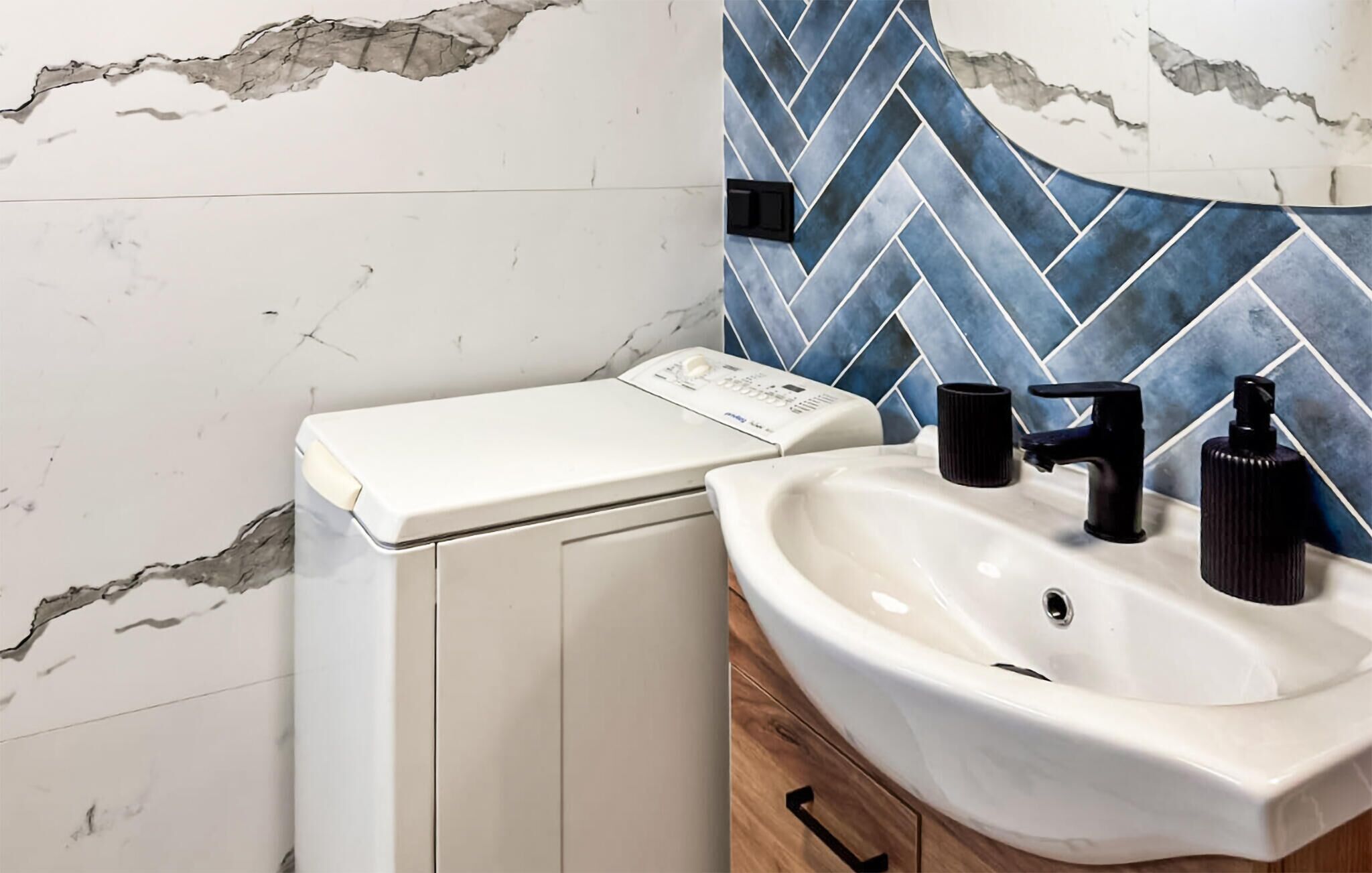 Un bany amb una rentadora blanca, un lavabo amb un aixeta negra i un rebedor blau i blanc.