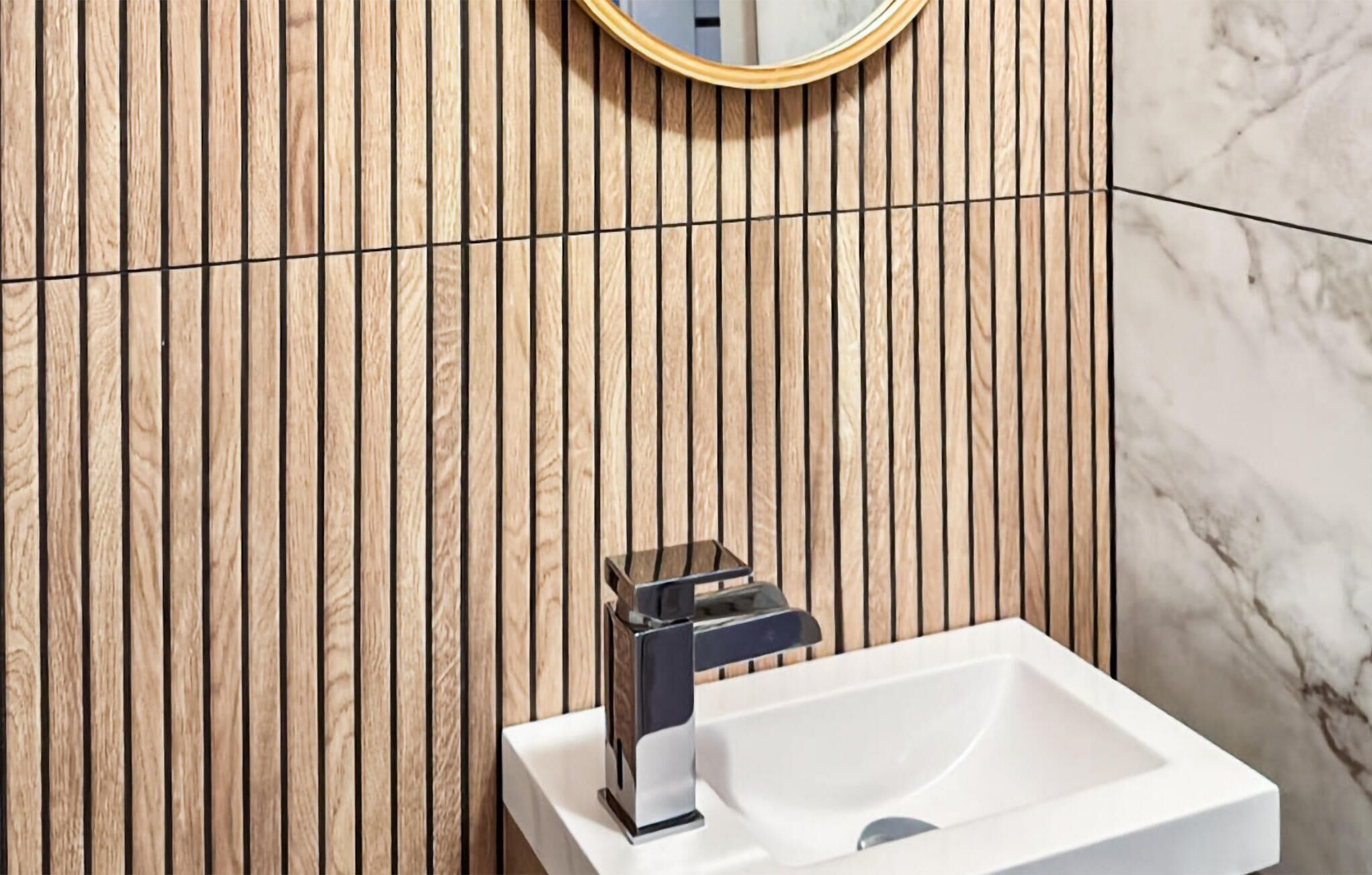 Une salle de bain avec un mur en lambris de bois, un lavabo blanc et un robinet moderne.