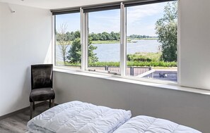 Une chambre avec une grande fenêtre donnant sur un lac et la verdure environnante.