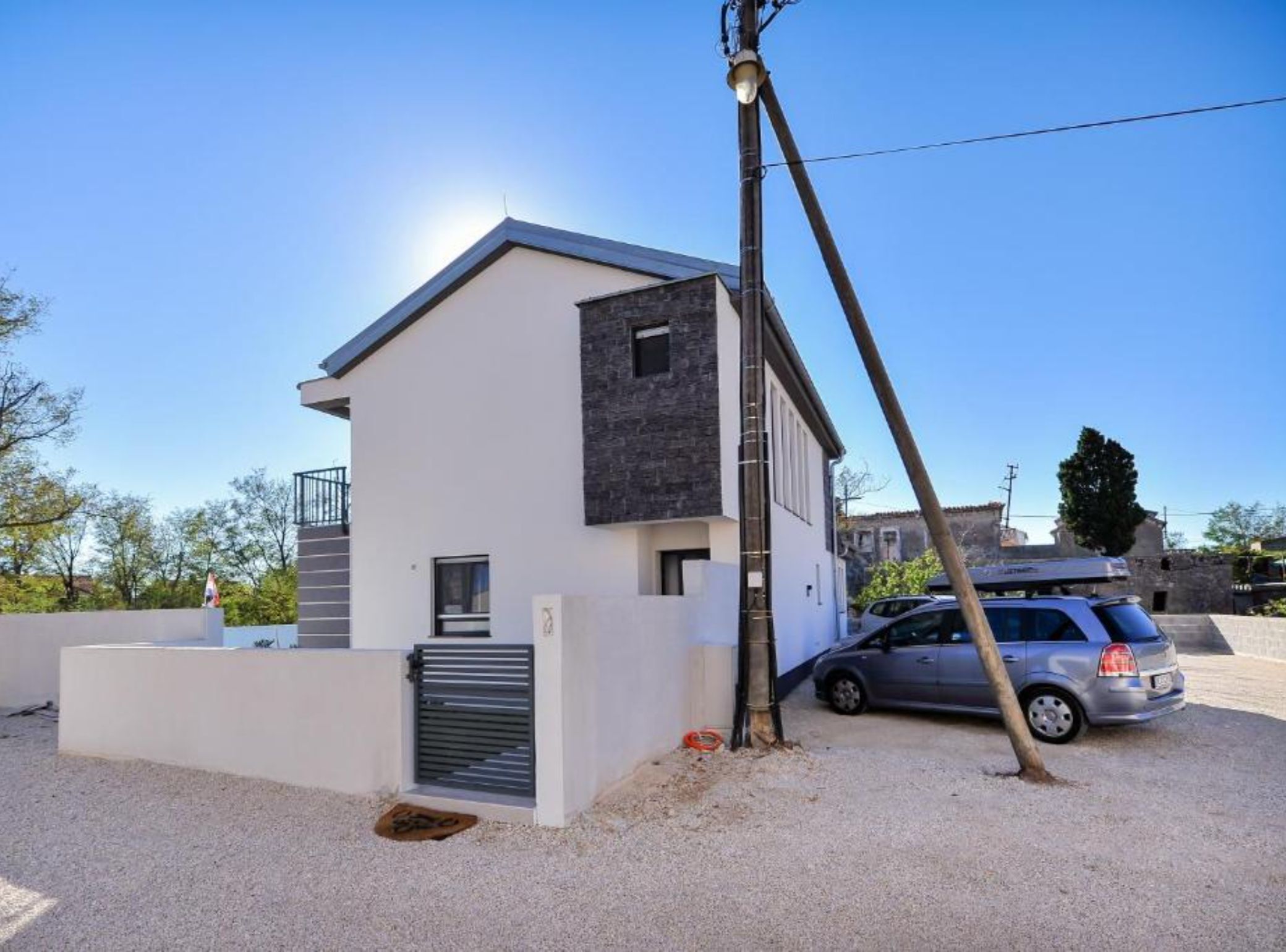 A modern two-story house with a flat roof, a small balcony, and a car parked in the driveway.