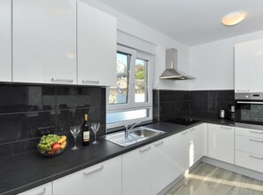 A modern kitchen with white cabinets, a black countertop, a window, and a stainless steel range hood. - Adriatic Villa Privlaka With Pool (Privlaka)