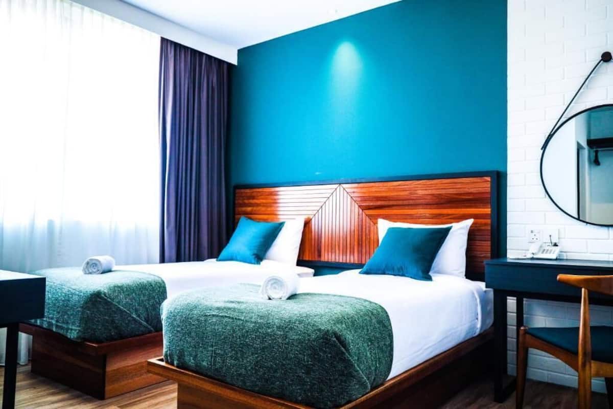 Habitación de hotel con dos camas, un escritorio, una silla y un espejo.