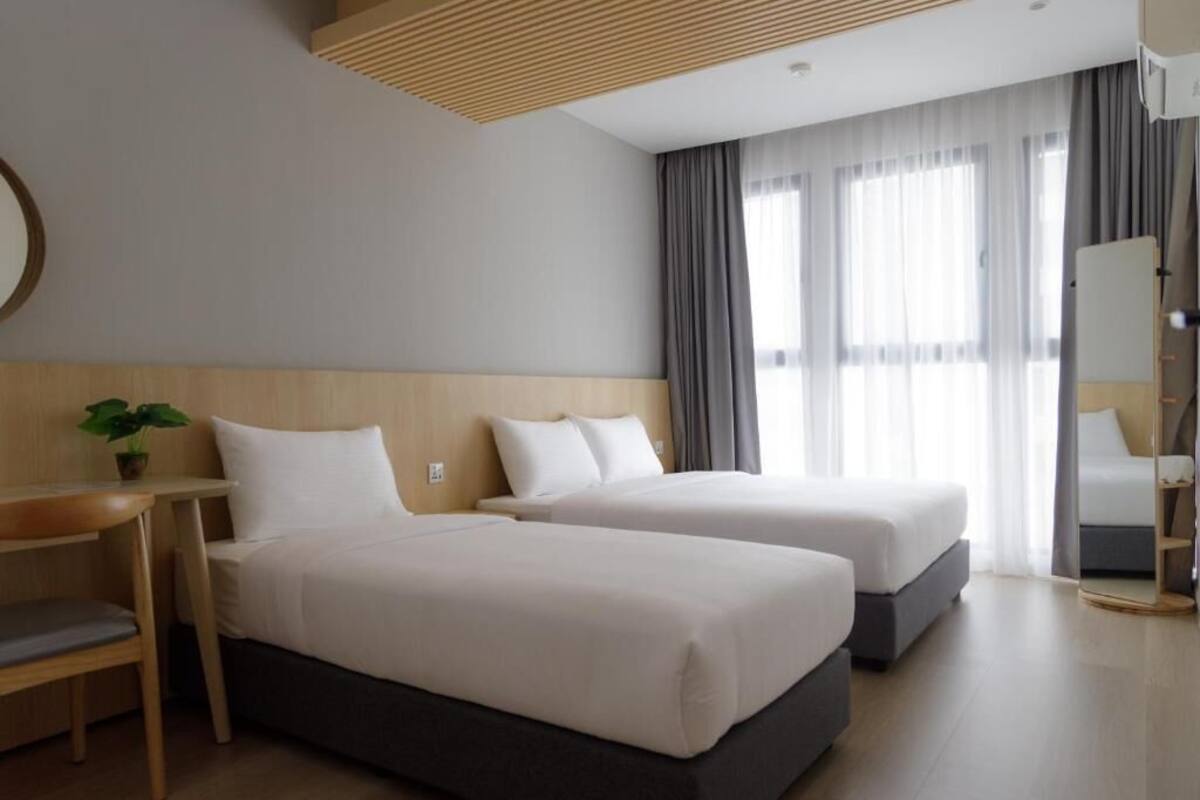 Una habitación de hotel con dos camas, un escritorio, una silla, una planta y un espejo.